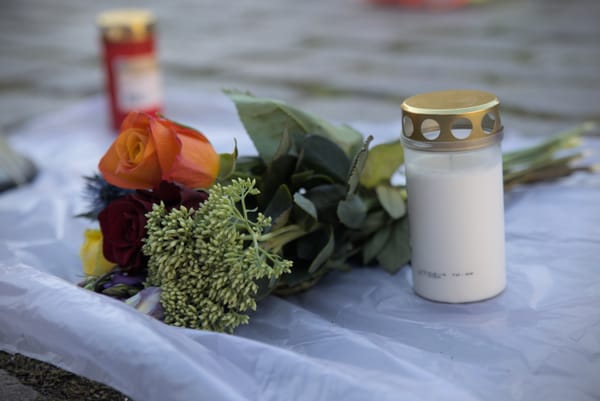 Photo eines Blumenstraußes und Grabkerzen auf eine Plastikfolie. Die Plastikfolie soll Wachs auffangen. Der Blumenstrauß ist in Regenbogenfarben gehalten.